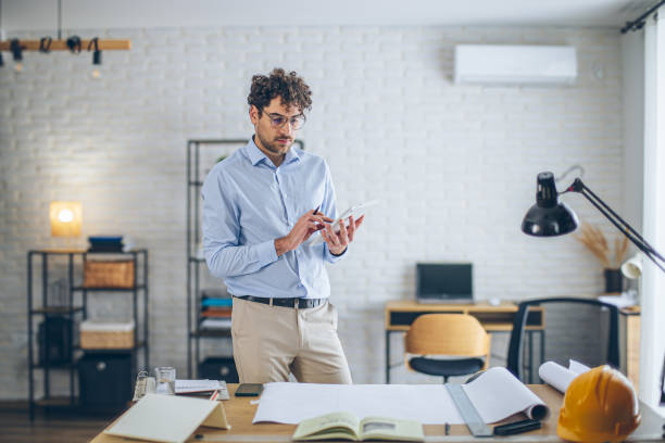 istock Modern architect working on tablet in bright modern office with blueprints on desk 2186666638