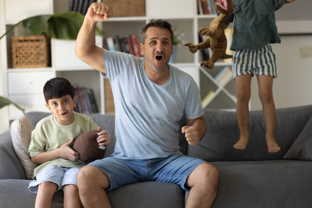 istock Boys watching soccer match with father at home, sitting on sofa 2186672185