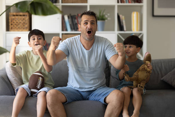 istock Boys watching soccer match with father at home, sitting on sofa 2186672272