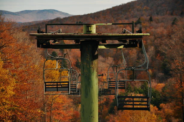 A green chairlift against mountains lined with orange autumn trees.