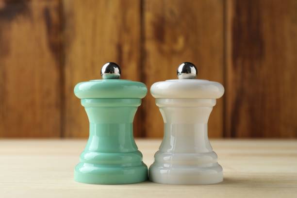 Salt and pepper shakers on light wooden table, closeup