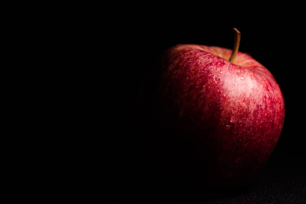 Partially Lit Red Apple in Silhouette on Black Background