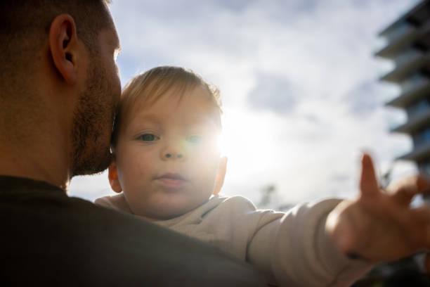Father gently embracing his son outdoor in the background is sky with sunlight