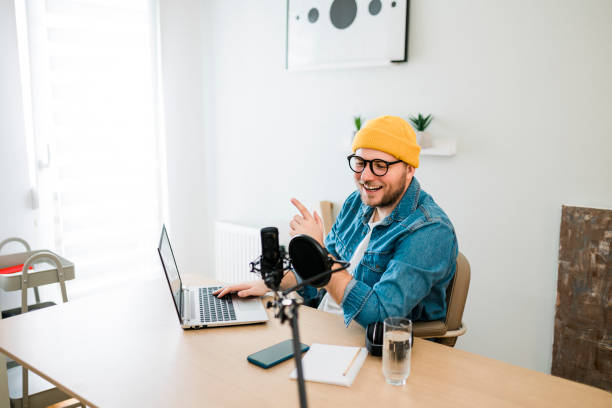 istock Young smiling man recording podcast and doing live streaming using microphone and headphones in recording studio 2186689049