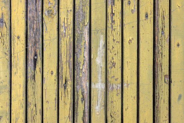 Old door boards with peeling yellow paint nailed with rusty nails.