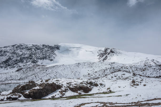 istock Dramatic cold alpine snow-white landscape with snow-capped peak of dome shape under cloudy sky. Snow-covered rocky mountain with snowy dome shaped top. Pure white snow and stones in high mountains. 2186697596