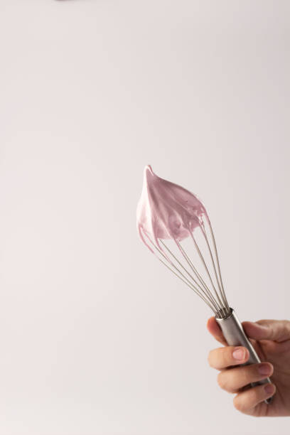 istock Whisk with pink frosting held by a hand against a neutral background for baking 2186703353