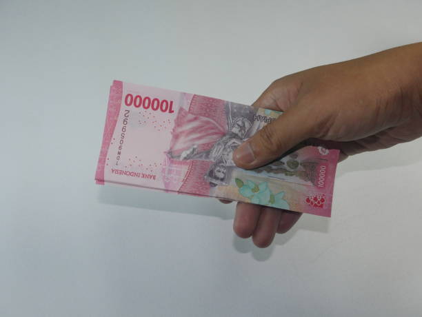 istock A crisp 100,000 Rupiah bill, carefully held in hand on a clean white background. 2186728346