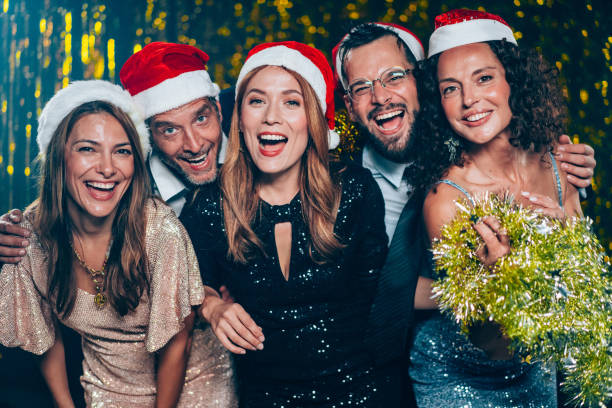 Portrait of cheerful group of friends with Santa hats embracing and looking at camera during Christmas party.