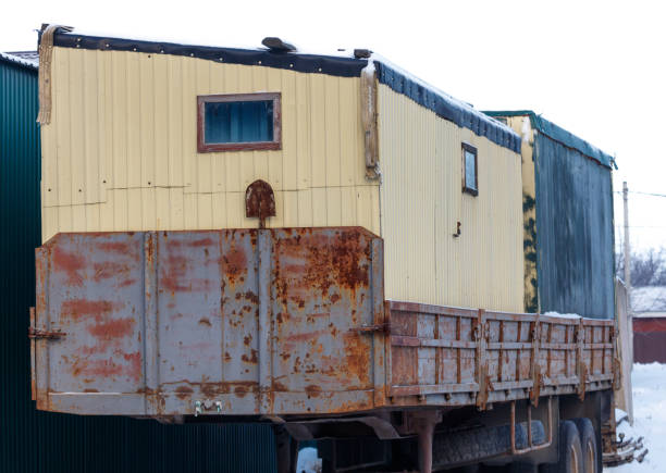 A rusted old truck with a yellow trailer attached to it. The trailer is covered in snow