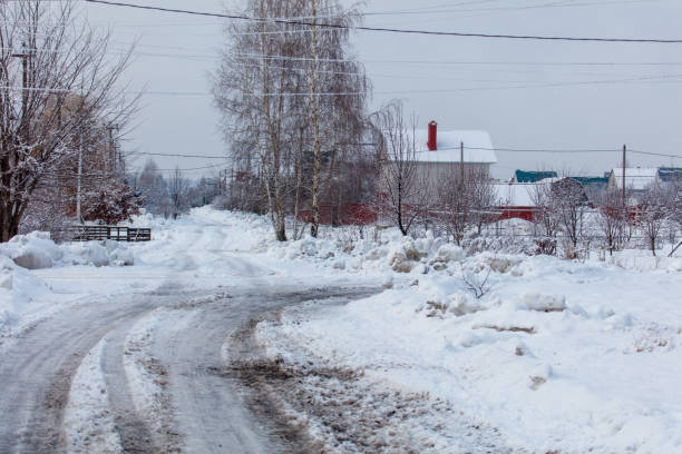 A snowy road with a house in the background. The road is covered in snow and has a lot of mud