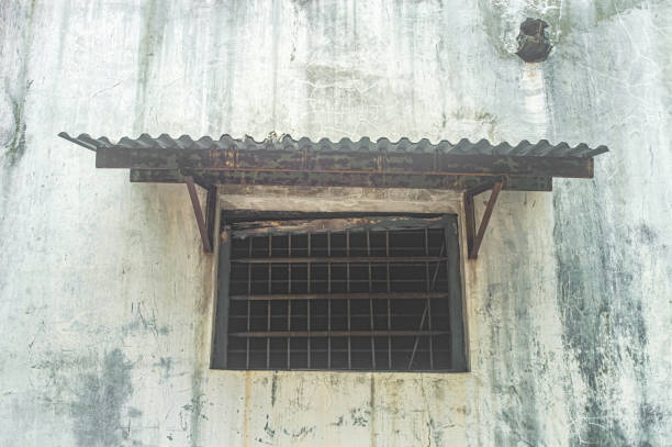 istock Old, weathered window with rusted metal bars and a corrugated iron awning on a dilapidated concrete wall. Ideal for themes of urban decay and rustic charm 2186736007