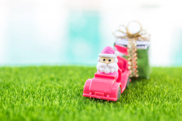 Miniature Santa Claus on pink plastic car with gift box over blurred background, Christmas concept background idea