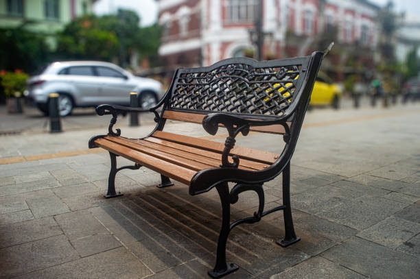 istock A beautifully designed park bench with intricate wrought iron armrests and backrest, set on a paved street with blurred background of cars and buildings, creating a serene urban scene 2186738378