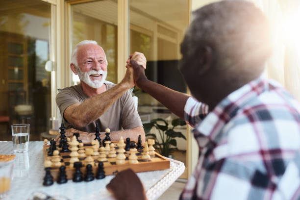 istock Happy senior men giving each other high-five while playing chess on a balcony. 2186738802