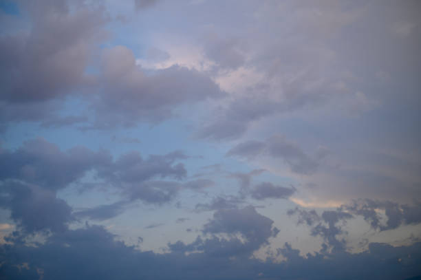 Dramatic clouds drift across a twilight sky, merging shades of blue and gray with hints of golden light
