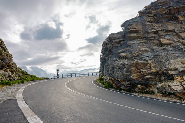 istock Beautiful road curve with nice asphalt on a mountain pass, carved between the two stone or rock walls. Nice clouds with sun in the background.. 2186739875
