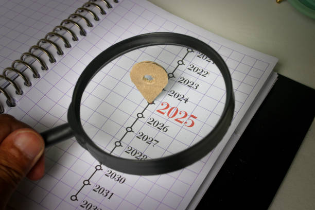 Hand Holding Magnifying Glass Focused on 2025 in Notebook
