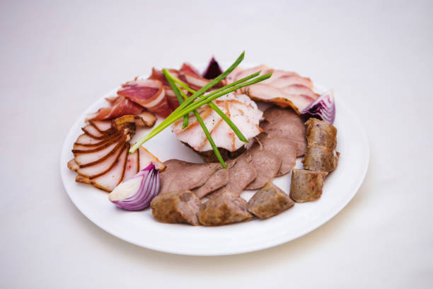 A plate of assorted meats and vegetables, including onions and celery, is arranged on a white table
