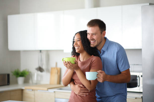 istock Happy interracial couple drinking and looking away in a kitchen 2186747838