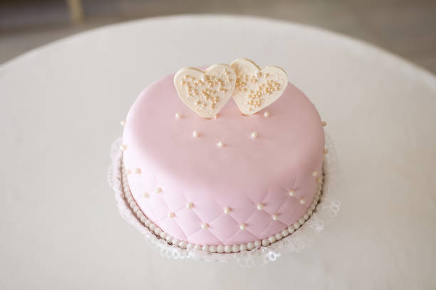 Stock photo shows a gracefully designed white wedding cake with smooth fondant icing rests on a refined silver stand. Captured from behind, the bride and groom toppers add a sentimental and artistic touch. Their delicate craftsmanship enhances the romantic essence