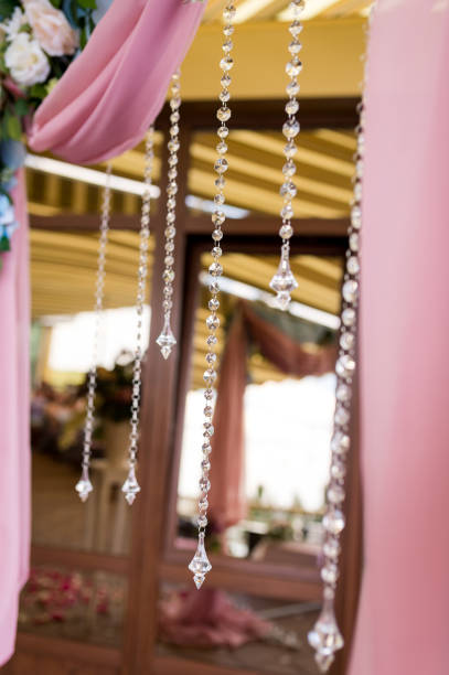 Elegant crystal decor hangs under pink drapery at a wedding venue. Crystal strands dangle beautifully from pink fabric in a wedding setting.