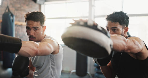 istock Men, personal trainer or boxer with practice at gym for training, exercise or workout together. Male person, fitness instructor or coach helping fighter with gloves for self defense at health club 2186755070