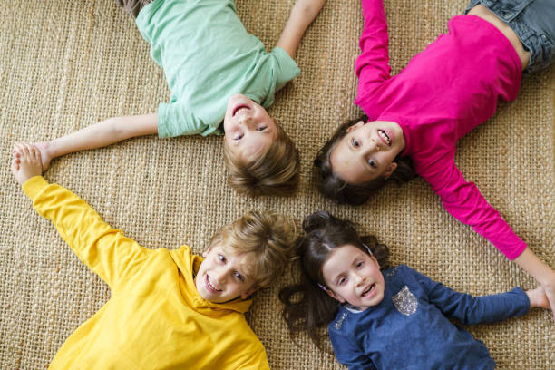 High angle view of group of happy children holding hands while lying in the circle on the floor