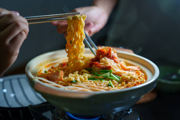 A person using chopsticks to pull delicious kimchi noodles from a hot pot. The bowl is filled with spicy kimchi, noodles, and fresh spring onions in a savory broth, creating a perfect meal for any occasion.