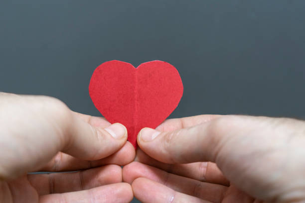 istock two hands holding a red paper heart in front of a black background 2186766535