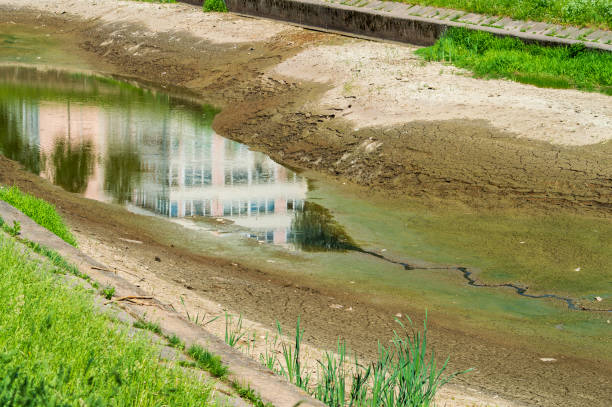 Bed of drying river or canal with building reflected in water