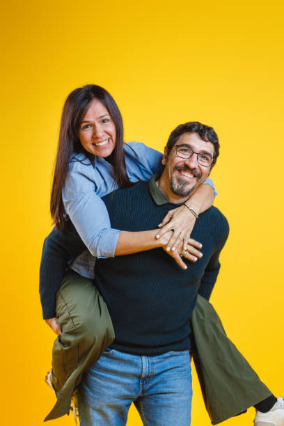 istock Joyful Couple Piggyback Ride on a Vibrant Yellow Background 2186772005