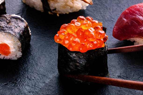 istock Sushi rolls on a black background. Ikura maki roll with chopsticks 2186773803