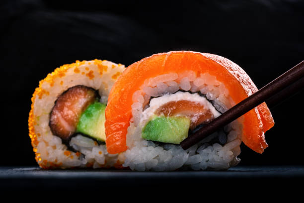 istock Two sushi rolls with salmon and avocado, on a black background with chopsticks 2186773811