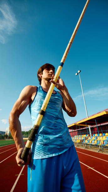 istock Pole jump athlete, focused young man in blue uniform standing with pole, showing reading for training session at open air stadium 2186776068