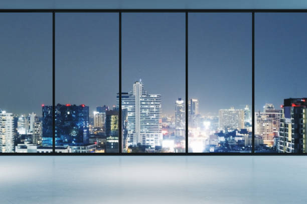 istock Large empty room with floor-to-ceiling windows overlooking a brightly lit city skyline at night. Business interior setting concept. 3D Rendering 2186776901