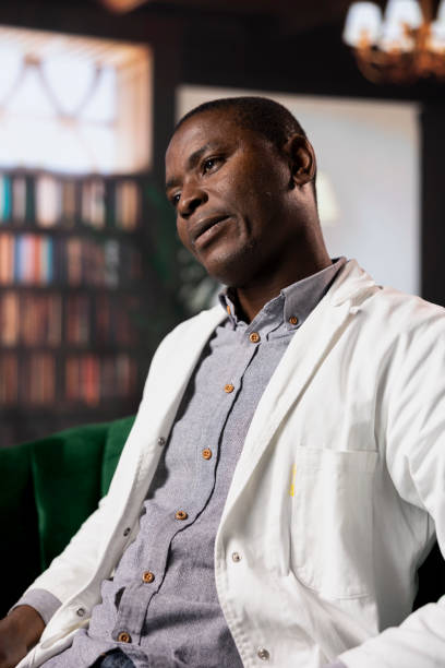 Black medic feeling overworked and deals with anxiety, sharing his PTSD feelings at counseling session. Doctor in consultation, receives support against depression and trauma.