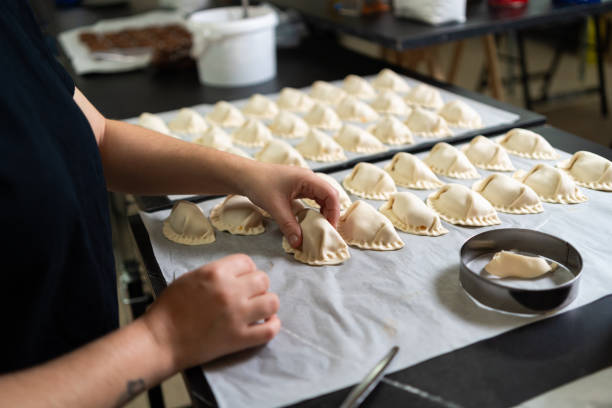 Experienced baker preparing empanadas and placing them on a baking sheet in a commercial kitchen