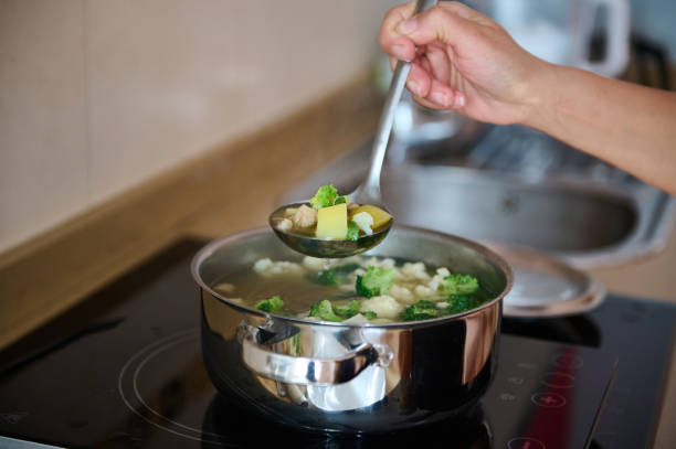 Close-up of a hand using a ladle to serve hot vegetable soup with broccoli and potatoes from a pot. Home cooking concept.