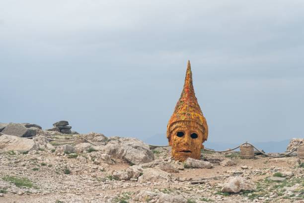 Ancient stone head with a pointed hat on Mount Nemrut, Turkey, under a cloudy sky, showcasing historical significance and unique landscape.