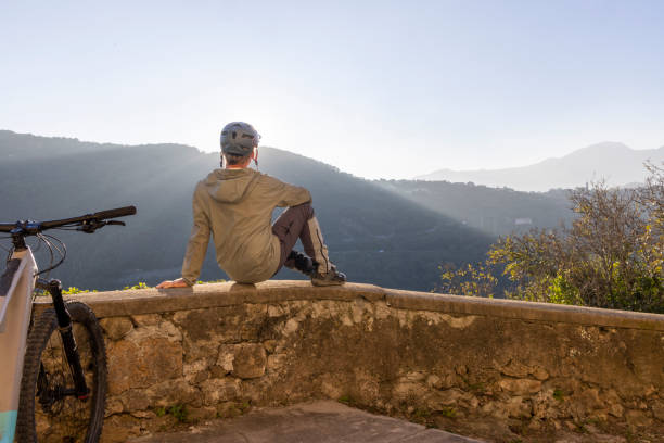 istock Mature mountain biker sits on rock wall above valley 2186779880
