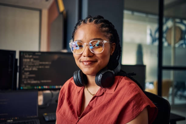 istock Young african american programmer smiling in modern office: sitting at desk and working on software development project 2186780914