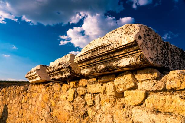 Ancient stone ruins under a vibrant blue sky with scattered clouds, showcasing historical architecture and texture.