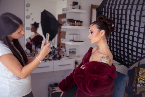 Make-up artist is helping the Beautiful woman to take a photo/video with her phone after applying makeup on her face
