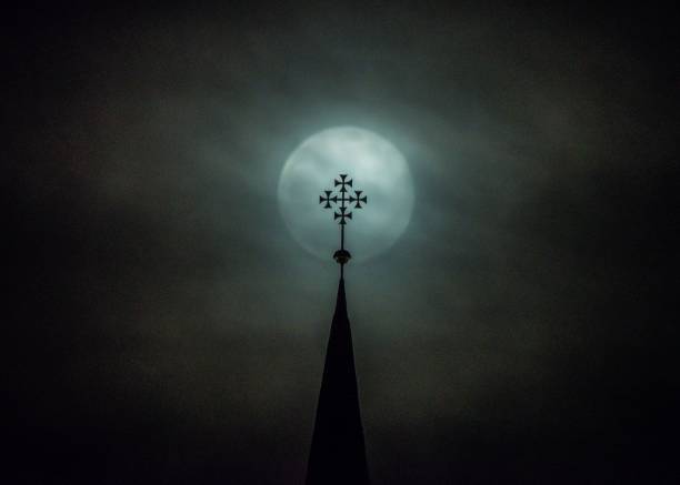 Full moon shines behind a church spire, casting a celestial glow on the cross