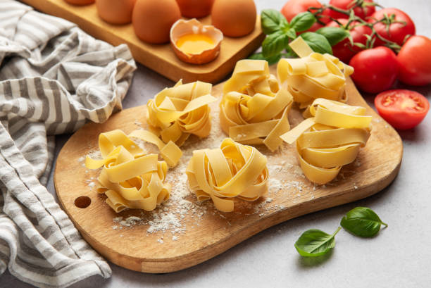 istock Uncooked tagliatelle pasta nests with basil, tomatoes and eggs on wooden cutting board 2186803662