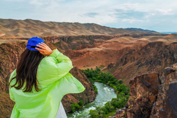Young woman traveler standing against the Black Canyon landscape. The Black Canyon is part of the Charyn Canyon and Charyn National Park. Located in the Almaty region in south-eastern Kazakhstan