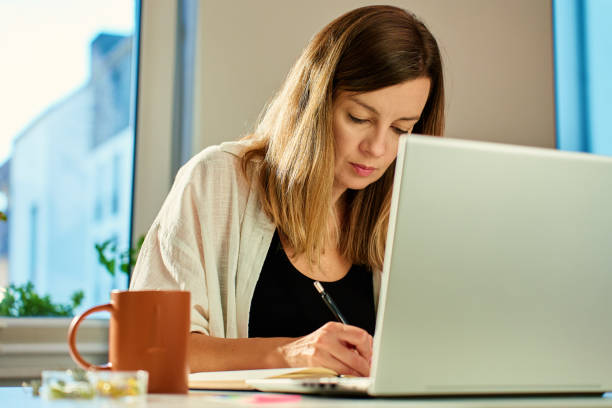 istock Woman working at home, writing in notebook and using laptop 2186807196