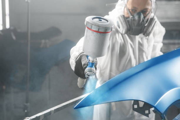 istock Car paint worker spraying blue paint to car body element using spray gun in vehicle workshop chamber. Complex restoration of automobile body. 2186812736