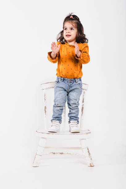 istock Little girl on a chair clapping her hands smiling on white background 2186817652